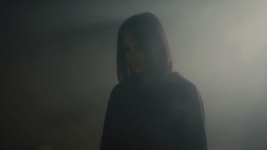Figura misteriosa envuelta en sombras y niebla.